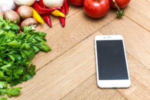 Smartphone liegt auf einem Holzbrett zwischen Gemüse