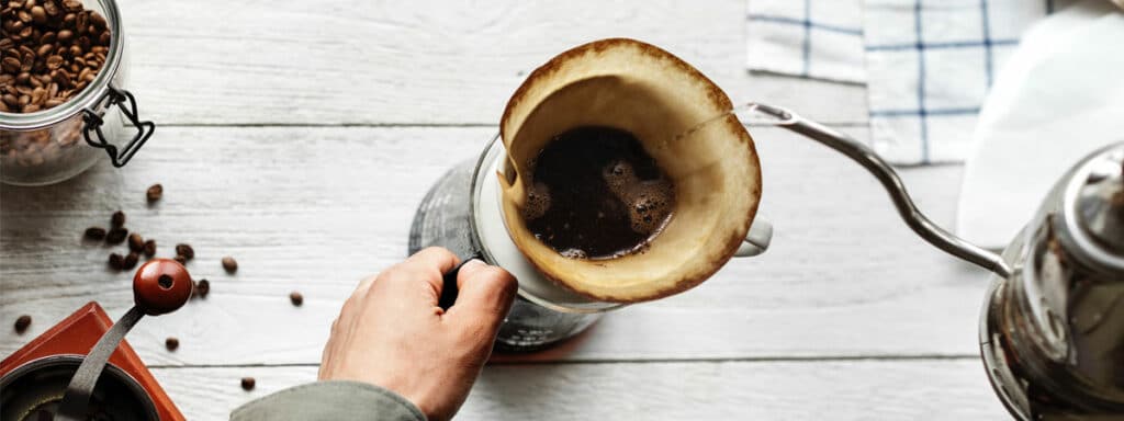 Tasse mit Kaffeefilter und gemahlenem Kaffee wird mit Wasser aufgegossen