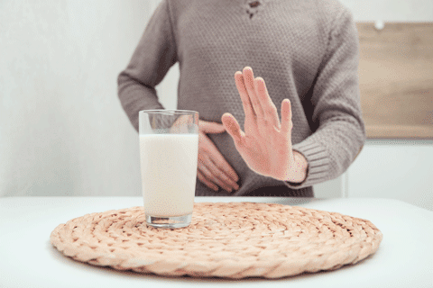 Mann hält sich den Bauch, vor ihm steht ein Glas Milch.