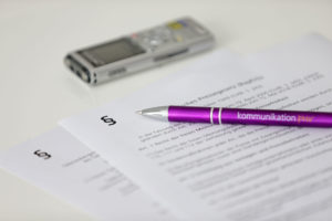 Ein Blatt Papier, ein Aufnahmegerät und ein Kugelschreiber liegen auf dem Tisch.