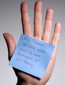 Eine Hand hält einen lila Zettel mit einem Zitat zu Kommunikation.
