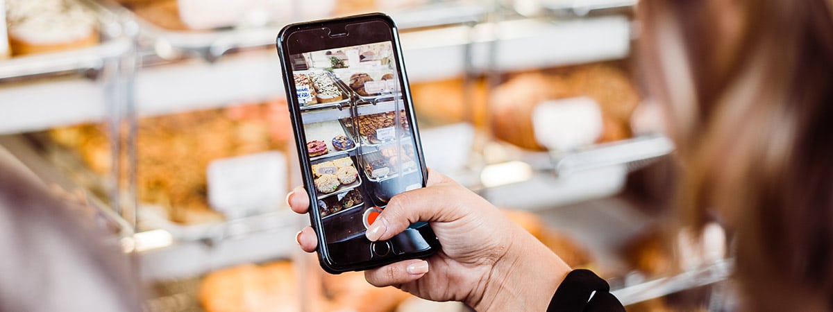 Frau macht Bild mit ihrem Handy von einer Bäckerei mit Brötchen